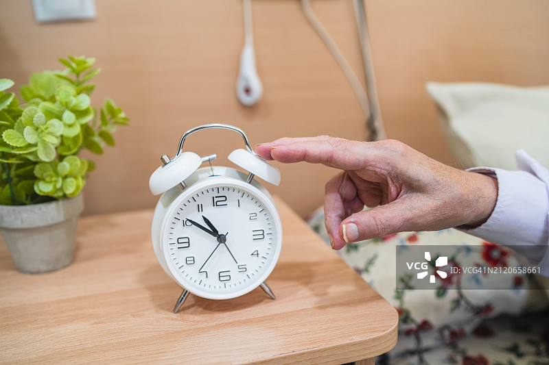 养老院里指着经典白色闹钟的年长老人之手图片素材