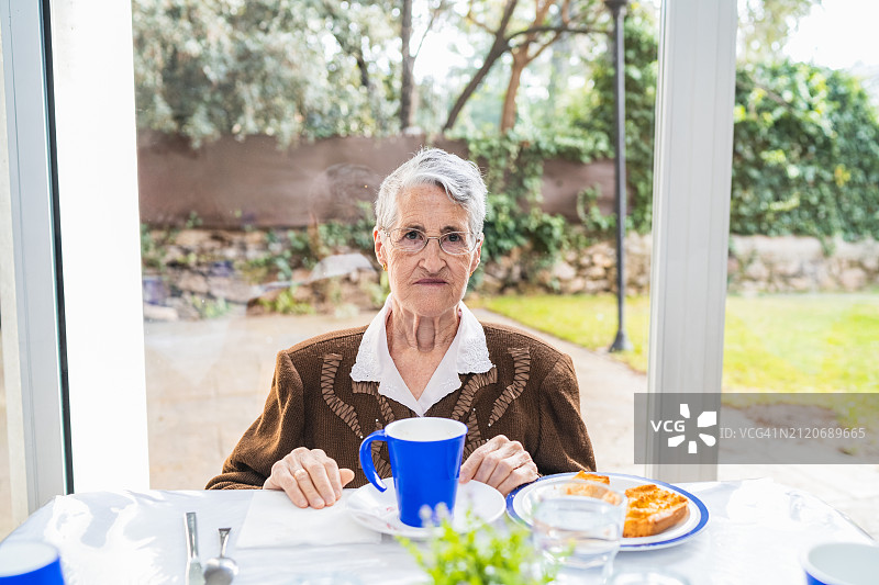 在护理院温室享用早餐的反光老年妇女图片素材