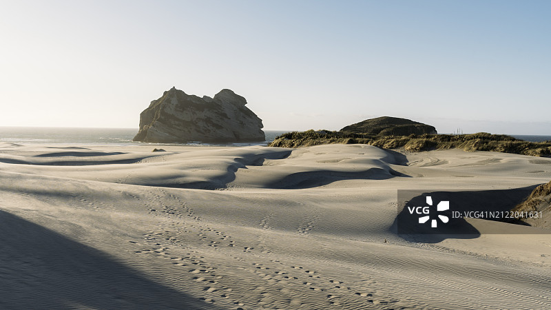 黄昏时柔和的阳光照亮海滩上的沙丘和海边的岩层图片素材