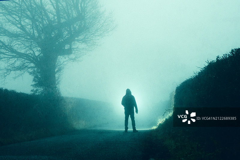 乡间雾夜，站在闹鬼道路上的阴森蒙面人图片素材