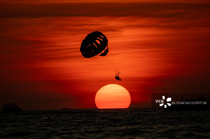 日落时分，迎着天空玩滑翔伞的人的剪影图片素材