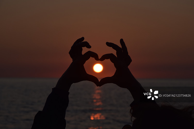 日落时分，双手在海边勾勒出心形轮廓图片素材