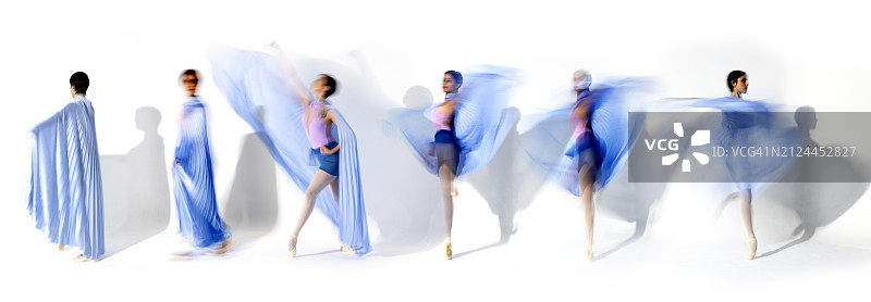 身穿蓝色裙子的年轻芭蕾舞演员在工作室灯光下跳舞，长曝光，白色背景图片素材