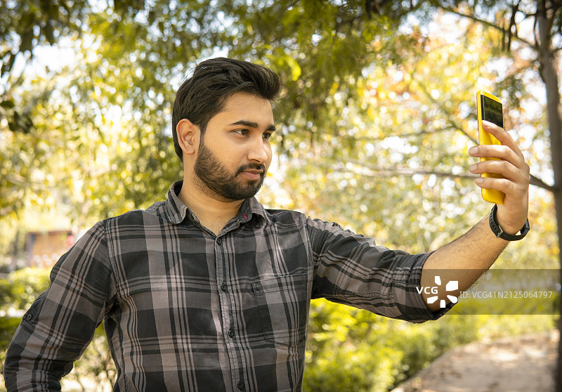印度年轻男子在享受大自然新鲜空气时用智能手机自拍的肖像图片素材