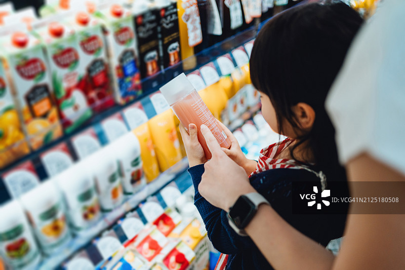 亚洲小女孩和妈妈在超市购物，在冷藏区拿着果汁，一起阅读营养标签图片素材