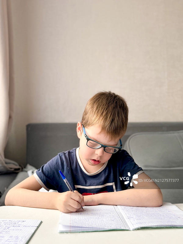 戴眼镜的10岁男孩坐在桌旁在家里写作业图片素材