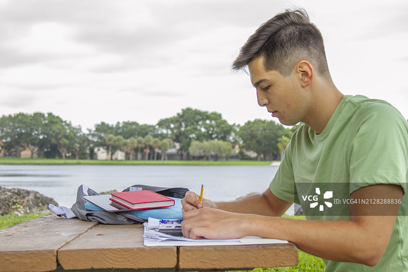 年轻的拉丁裔大学生，快乐英俊的男大学生，在大学校园图书馆外，欣赏壮观的湖景，做家庭作业图片素材
