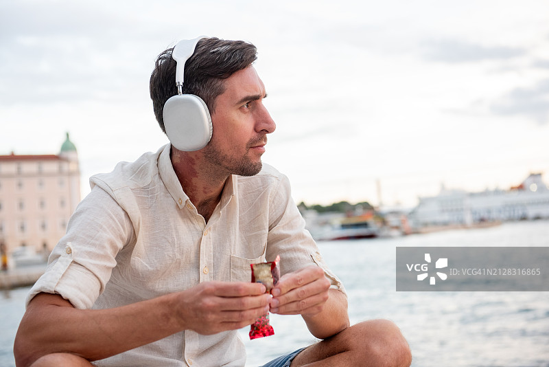 脖子上戴着大耳机和红色胎记的年轻男子打开KitKat Chunky牛奶巧克力图片素材