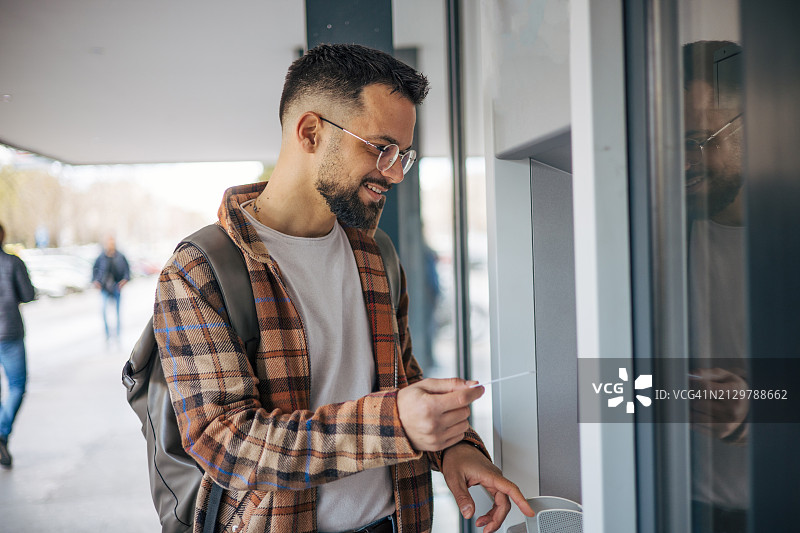 英俊男人使用信用卡从自动取款机取款图片素材