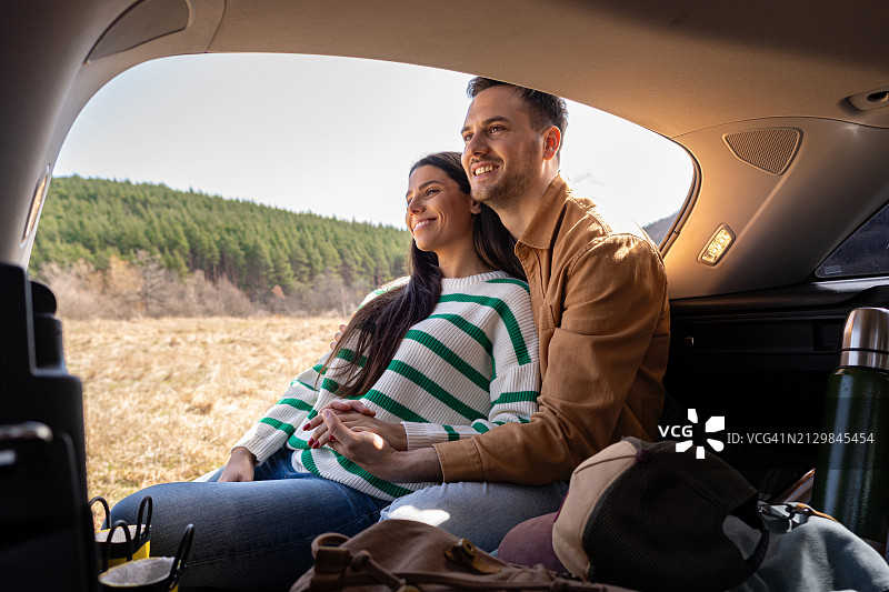 年轻情侣坐在汽车后备箱里，享受大自然图片素材