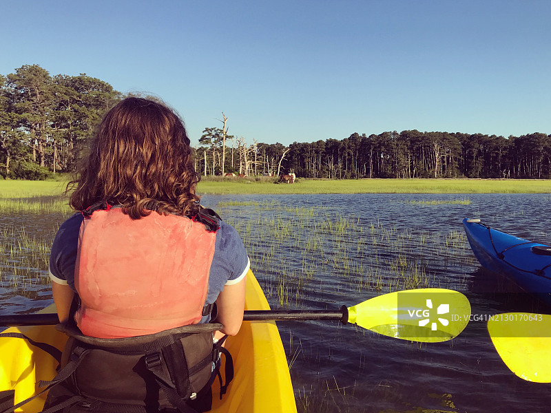 女孩划皮艇观看钦科蒂格岛附近的野生小马，周末度假图片素材