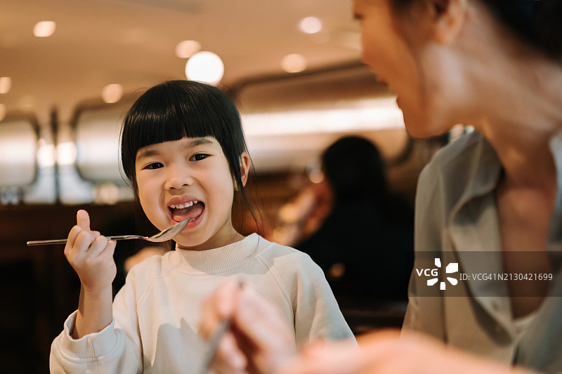 可爱的亚洲小女孩和妈妈在餐厅愉快用餐，母女俩边吃边聊，享受亲子时光，美食与生活图片素材