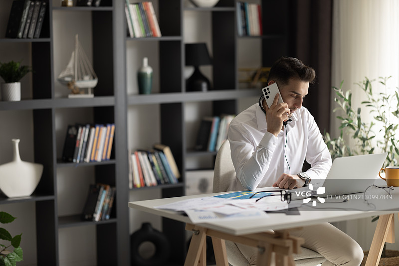 在家办公室内使用智能手机通话的年轻英俊商人图片素材