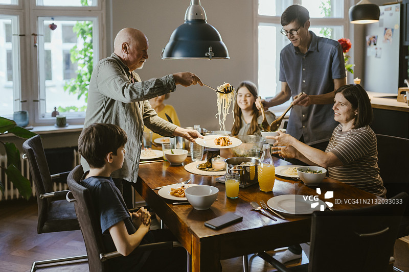 在家吃晚饭时为家人提供面条的年长男人图片素材