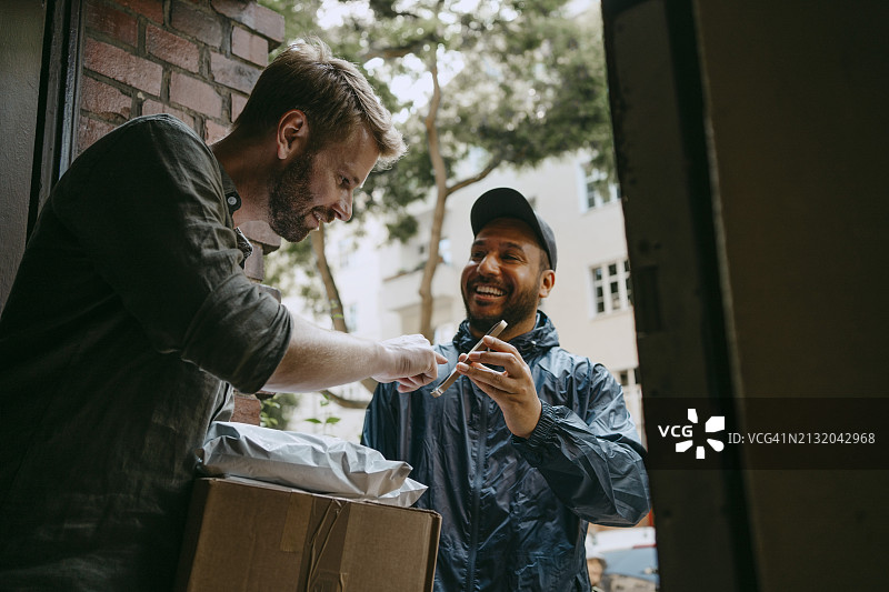 微笑的送货员向男子收取电子签名并交付包裹图片素材