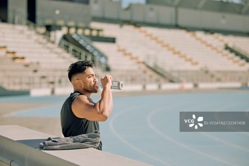 体育场内跑步训练的疲惫男人：马拉松运动员的补水、锻炼与健康图片素材