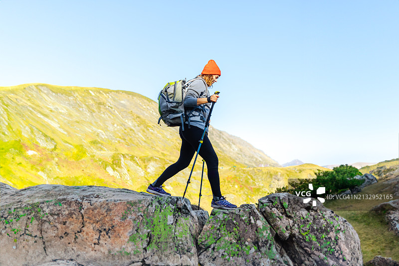 一位戴着橙色帽子的徒步女性使用登山杖在山区地形中跋涉图片素材