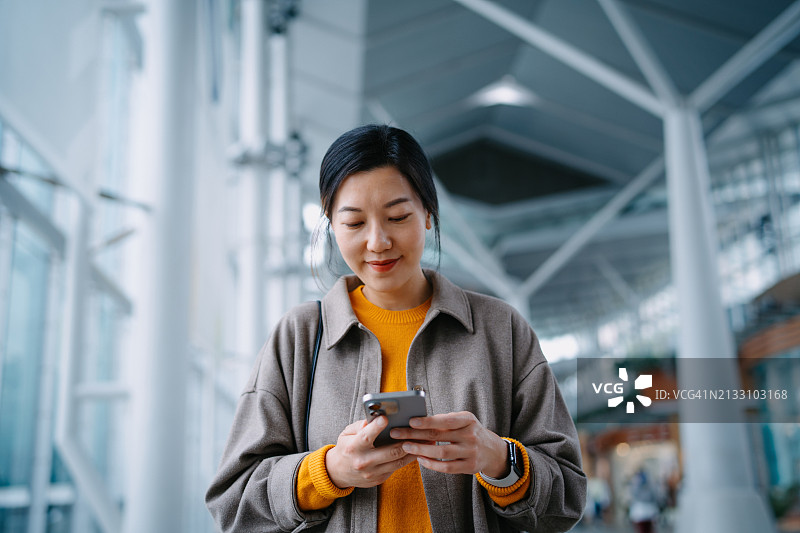 在购物中心里使用智能手机的亚洲年轻女子图片素材