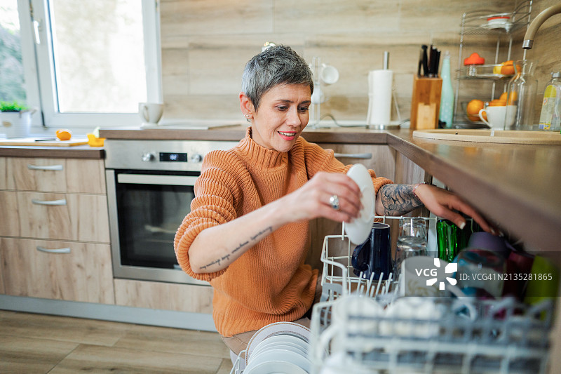 在厨房卸洗碗机的中年妇女图片素材