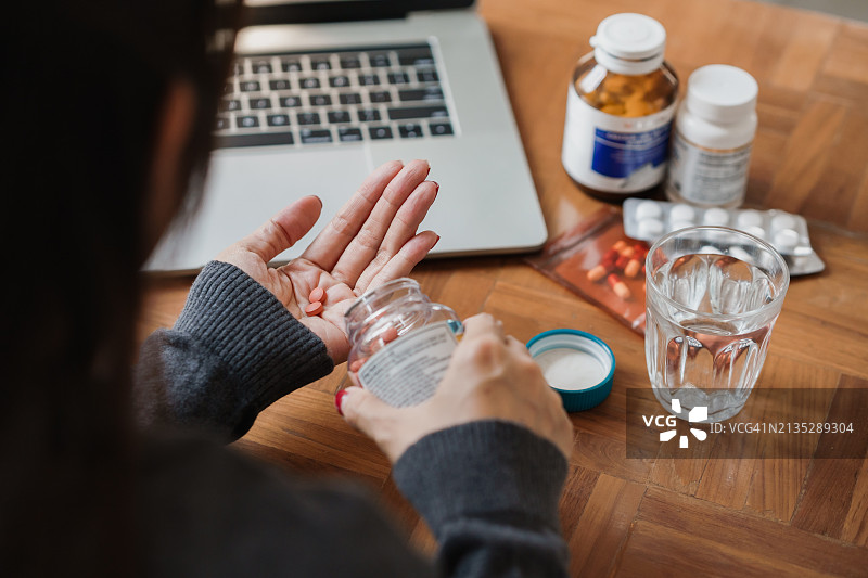 感到不适，手拿药丸和一杯水的亚洲女性背影。在家治疗常见疾病。家庭医疗保健。图片素材