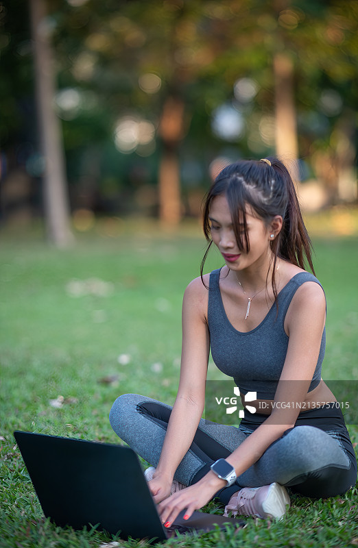 年轻漂亮的亚洲女子在公园草地上使用笔记本电脑图片素材