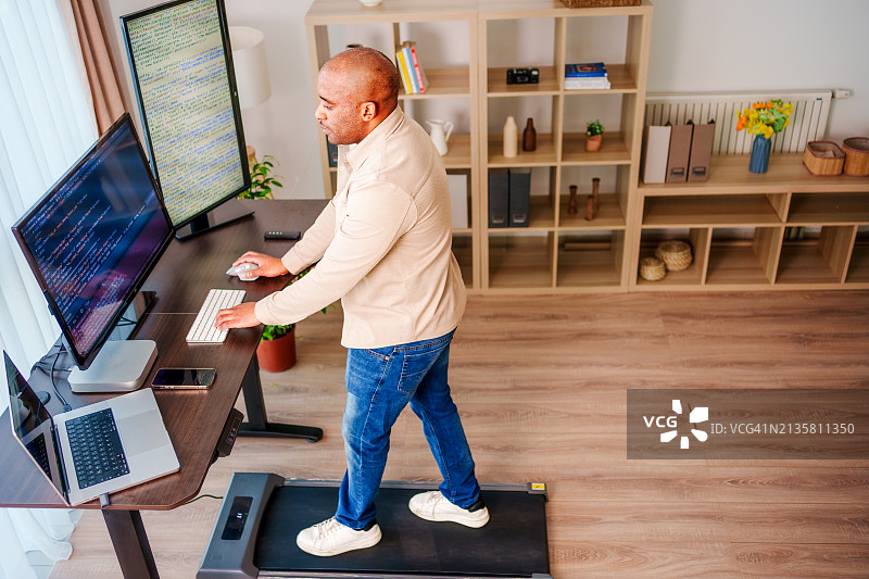 在家办公并在桌下跑步机上行走的黑人男子图片素材