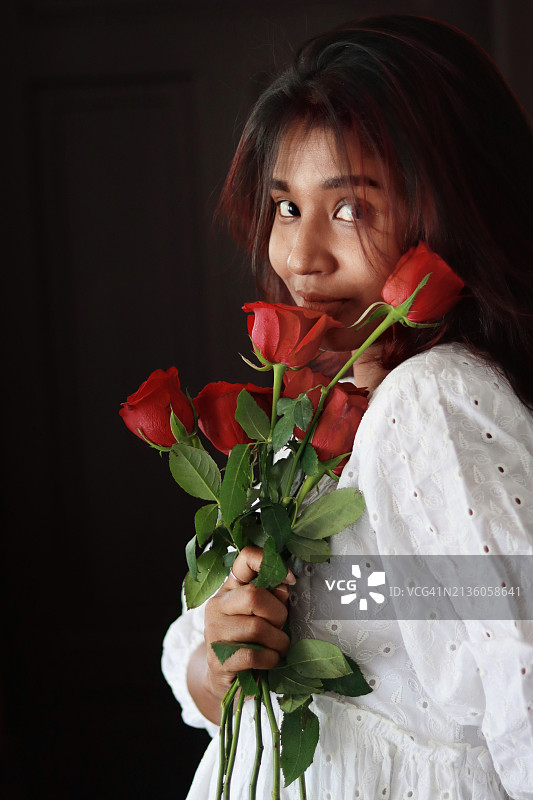 在黑色背景下手持玫瑰的女人肖像，印度喀拉拉邦特里凡得琅图片素材