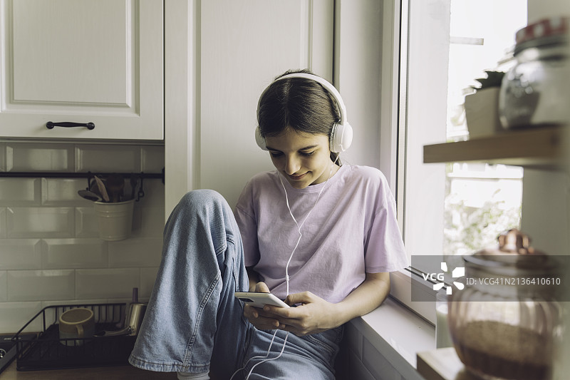 在厨房台面上戴着耳机的美丽女孩图片素材