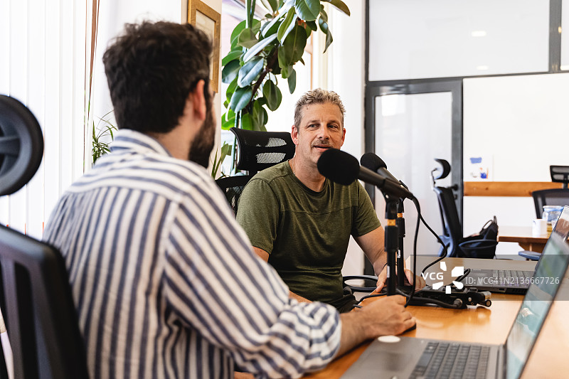 两位金融专家在明亮的办公室里用笔记本电脑和专业麦克风记录讨论图片素材