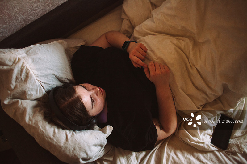 年轻女人躺在床上戴着耳机听音乐图片素材