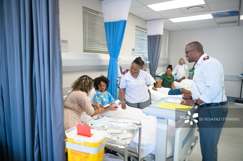 友善的医务人员与年轻非洲女孩及其母亲在医院病房的病床上一起读书图片素材