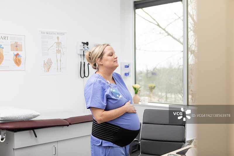 怀孕的外科医生闭着眼睛，通过宫缩进行呼吸图片素材