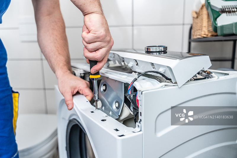 维修工用螺丝刀拆卸洗衣机进行维修图片素材