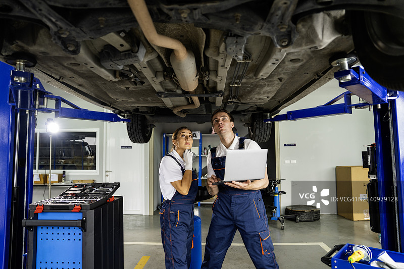 两位技术人员在汽车维修店检查车辆底盘和悬挂系统图片素材