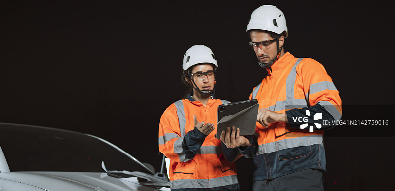 白人男女工程师在户外工地协同工作，使用平板电脑在车旁讨论。加班，过度劳累，工程技术概念图片素材