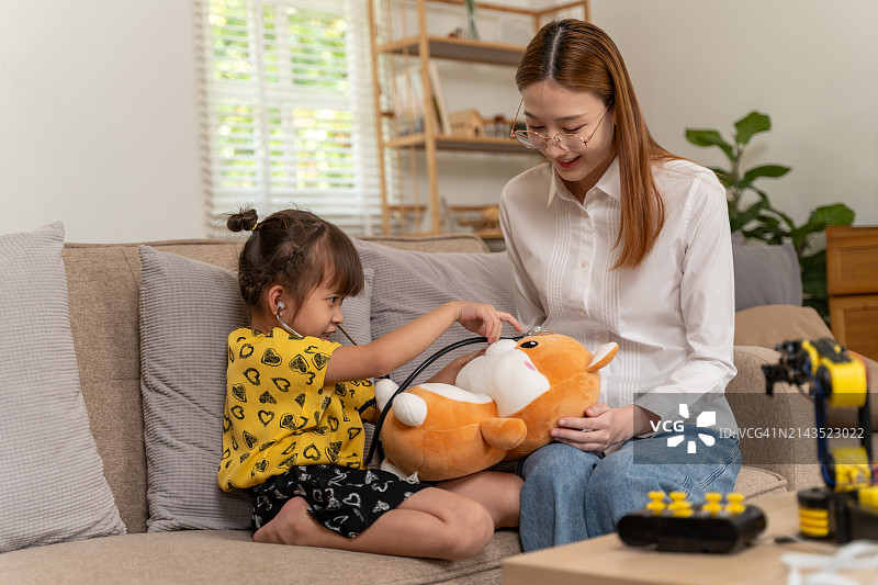 小女孩在客厅里用玩具听诊器给泰迪熊看病图片素材
