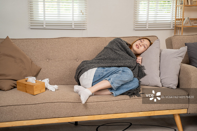 年轻生病的女子在客厅沙发上睡觉，旁边放着一盒纸巾图片素材