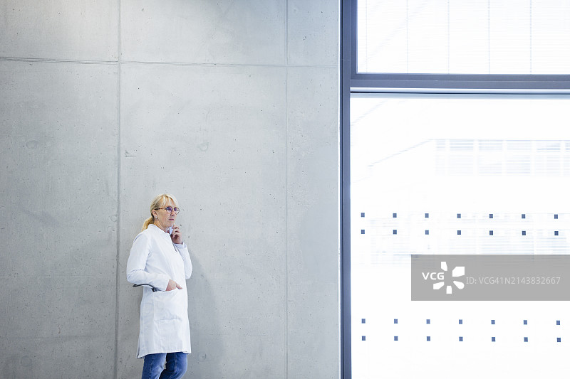 年长的医生在墙边用手机通话图片素材