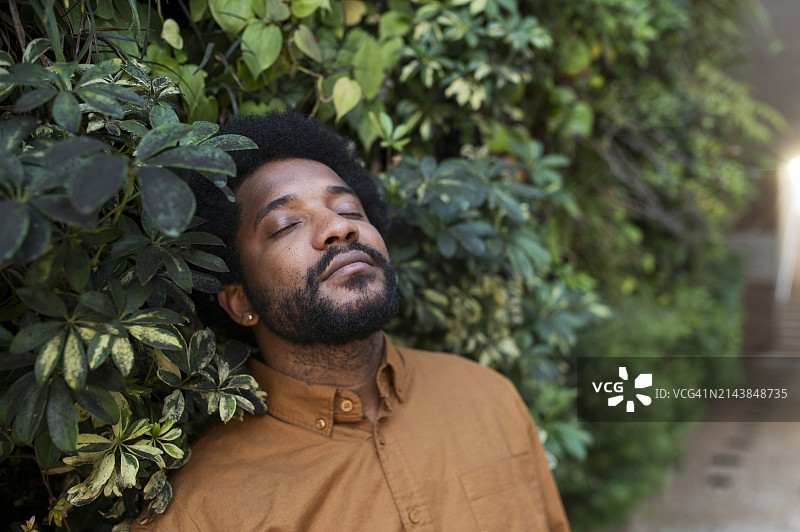 在植物附近闭着眼睛的年轻男人图片素材