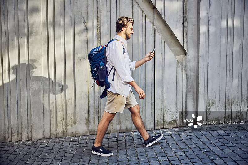 年轻男子背着背包在人行道上使用智能手机图片素材