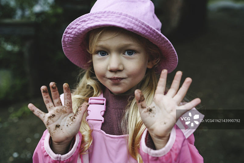 穿着粉色雨衣和帽子，展示脏手的女孩图片素材