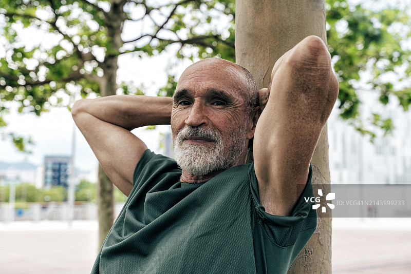 双手放在脑后在树干上放松的退休老人图片素材