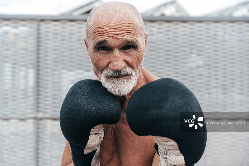 自信的袒胸年长男人戴着拳击手套练习图片素材