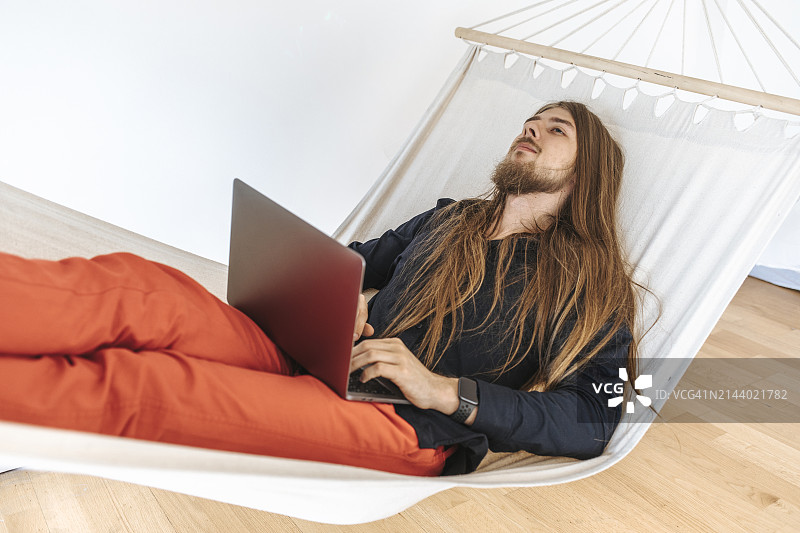 年轻程序员在办公室创业公司的吊床上用笔记本电脑放松图片素材