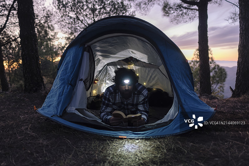 男人在帐篷里戴着头灯看书图片素材