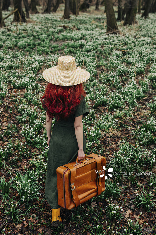 女士拉着复古手提箱穿过森林里的铃兰花图片素材