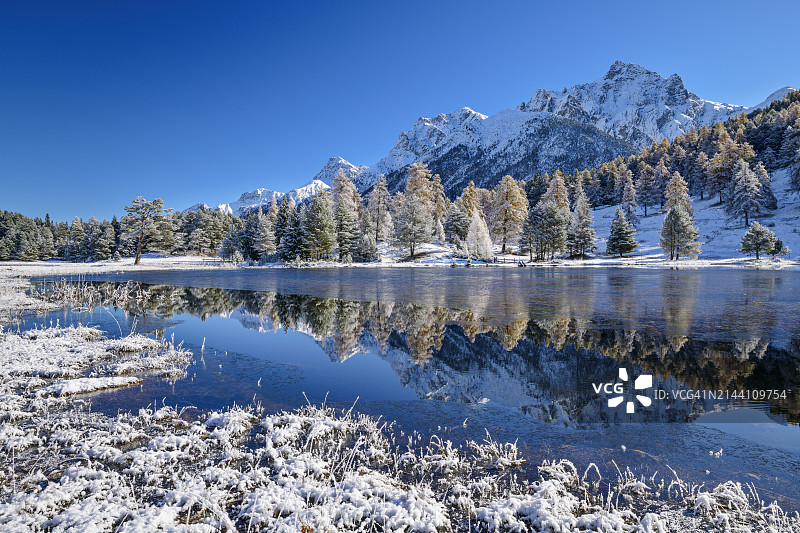 阳光明媚，瑞士格里松州下恩嘎丁地区塔拉斯普附近的雪山阿尔卑斯山湖泊倒影图片素材