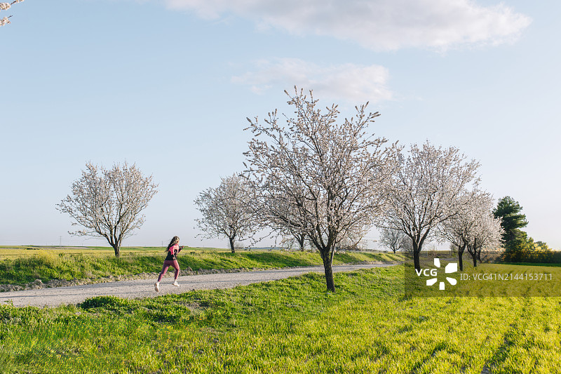 女人在杏花盛开的草地附近的人行道上跑步图片素材