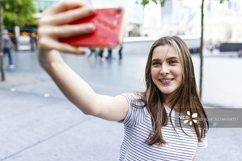 在人行道上用智能手机自拍的微笑年轻女人图片素材