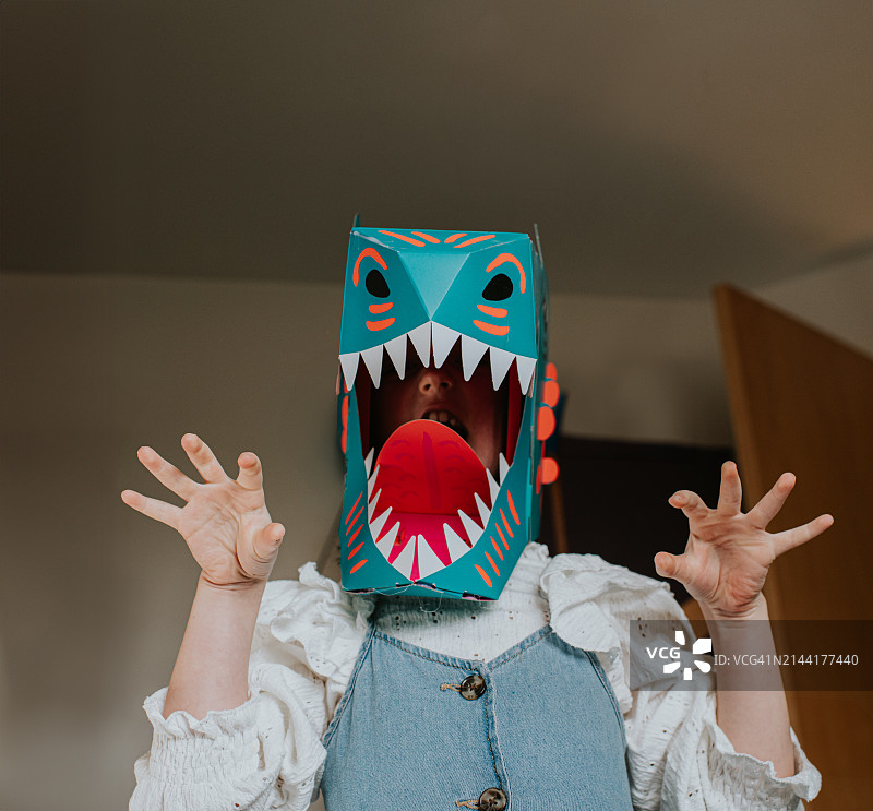 一个戴着自制纸板恐龙面具的孩子，摆出凶猛的姿势，朝着镜头咆哮图片素材